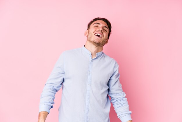 Il giovane uomo caucasico che posa in una parete rosa ha isolato la risata rilassata e felice, il collo allungato mostrando i denti.