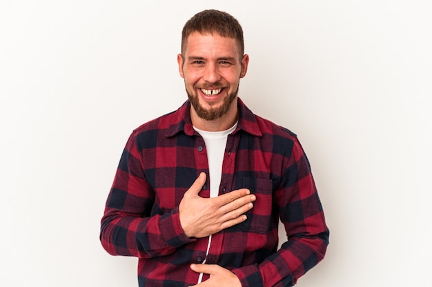 Il giovane uomo caucasico con diastema isolato su sfondo bianco ride felicemente e si diverte a tenere le mani sullo stomaco.