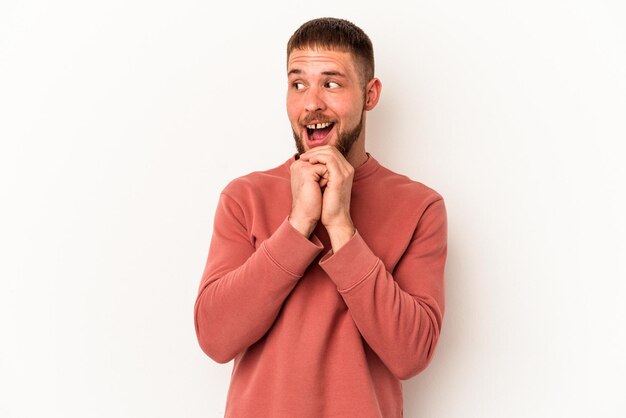 Il giovane uomo caucasico con diastema isolato su sfondo bianco tiene le mani sotto il mento, sta guardando felicemente da parte.