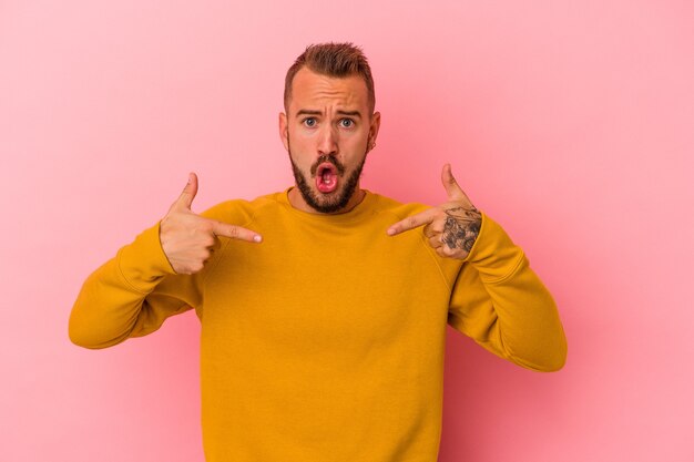 Il giovane uomo caucasico con tatuaggi isolati su sfondo rosa punta verso il basso con le dita, sensazione positiva.