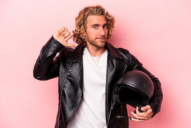 Il giovane uomo caucasico con un casco da motociclista isolato su sfondo rosa si sente orgoglioso e sicuro di sé, esempio da seguire.