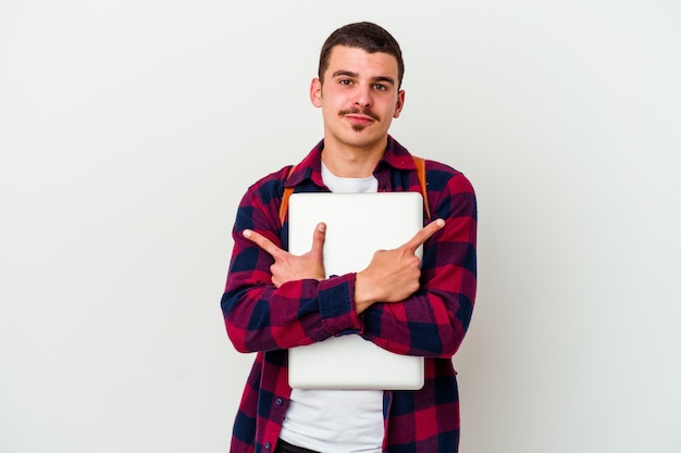 Il giovane uomo caucasico dell'allievo che tiene un laptop isolato sui punti bianchi lateralmente, sta provando a scegliere fra due opzioni.