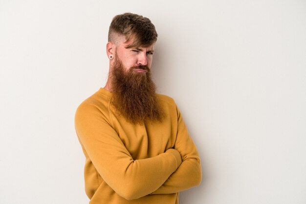 Il giovane uomo caucasico dello zenzero con la barba lunga isolato sul fronte bianco accigliato nel dispiacere, tiene le braccia conserte.