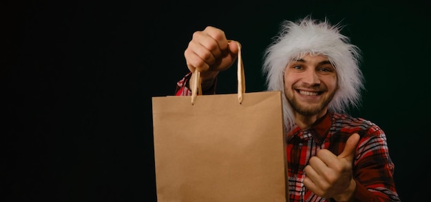 Il giovane uomo caucasico in cappello rosso di Babbo Natale tiene un pacchetto artigianale ecologico