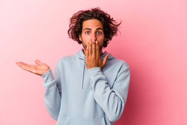 Il giovane uomo caucasico isolato su bakcground rosa ha impressionato tenendo lo spazio della copia sul palmo.