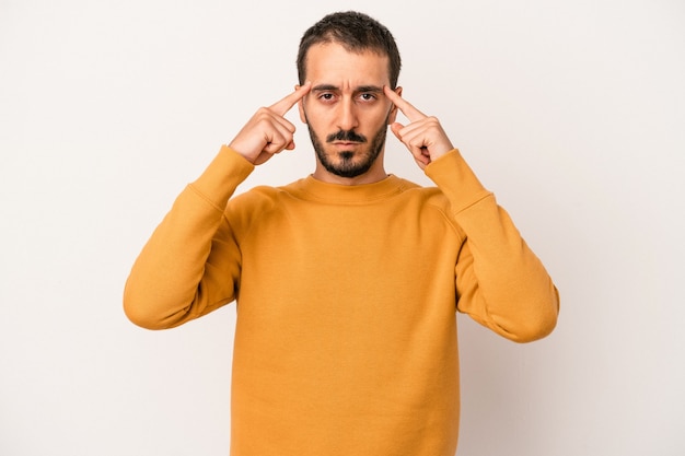 Il giovane uomo caucasico isolato su sfondo bianco si è concentrato su un compito, tenendo gli indici puntati verso la testa.