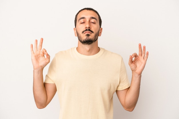 Il giovane uomo caucasico isolato su sfondo bianco si rilassa dopo una dura giornata di lavoro, sta eseguendo yoga.