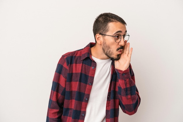 Il giovane uomo caucasico isolato su sfondo bianco sta dicendo una notizia segreta di frenata calda e sta guardando da parte