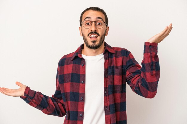 Il giovane uomo caucasico isolato su sfondo bianco tiene lo spazio della copia su un palmo, tiene la mano sulla guancia. Stupito e deliziato.