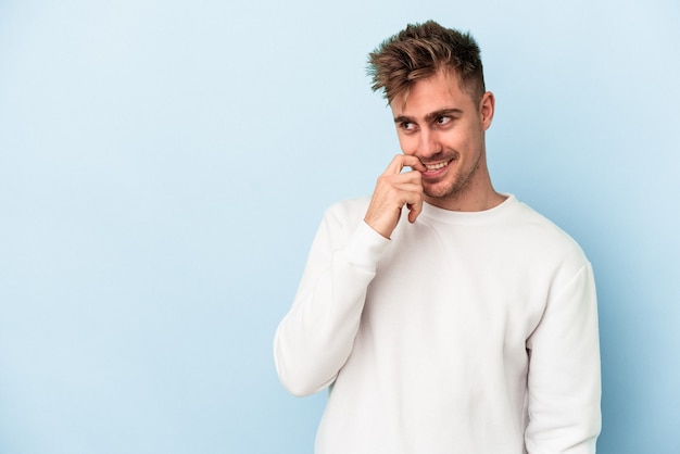 Il giovane uomo caucasico isolato su sfondo blu si è rilassato pensando a qualcosa guardando uno spazio di copia.