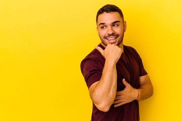 Il giovane uomo caucasico isolato su sfondo giallo indica con il pollice lontano, ridendo e spensierato.