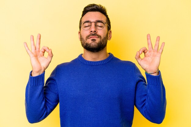 Il giovane uomo caucasico isolato su sfondo giallo si rilassa dopo una dura giornata di lavoro che sta eseguendo yoga