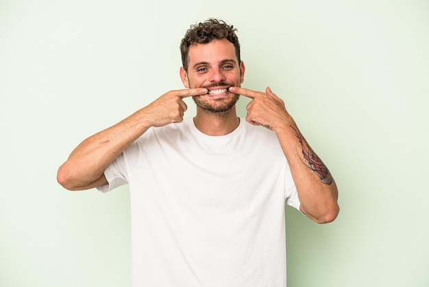 Il giovane uomo caucasico isolato su sfondo verde sorride, puntando il dito alla bocca.