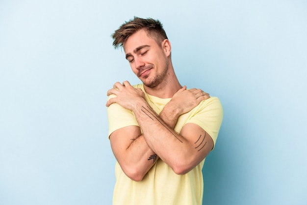 Il giovane uomo caucasico isolato sugli abbracci blu del fondo, sorride spensierato e felice.