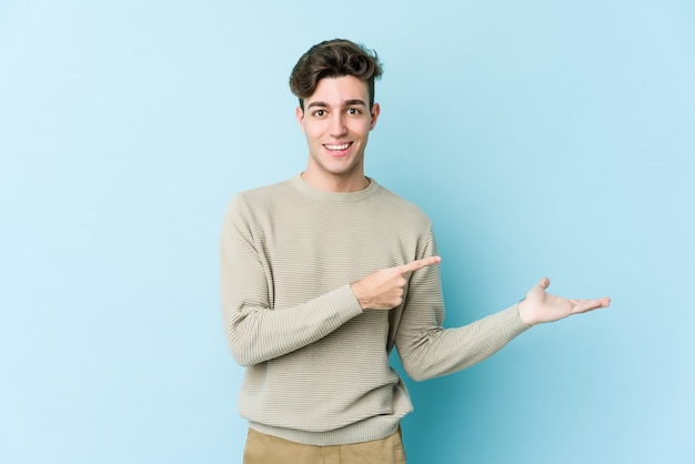 Il giovane uomo caucasico isolato sulla parete blu ha eccitato tenendo uno spazio della copia sul palmo.