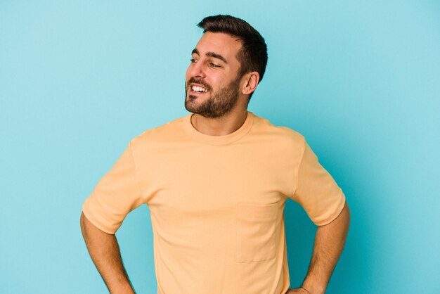 Il giovane uomo caucasico isolato sulla parete blu ride allegramente e si diverte a tenere le mani sullo stomaco