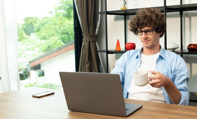 Il giovane uomo caucasico lavora da casa sul laptop e si connette online all'ufficio al chiuso per il posto di lavoro Internet remoto