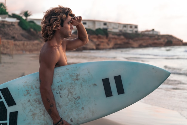 Il giovane uomo caucasico si alza presto per fare surf all'alba