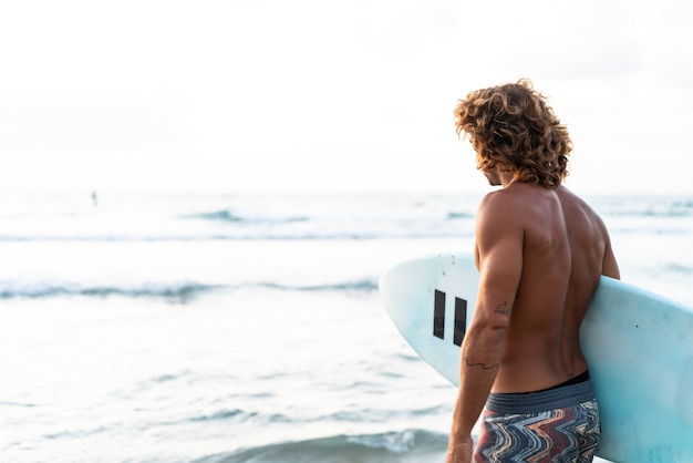 Il giovane uomo caucasico si alza presto per fare surf all'alba