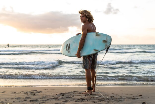 Il giovane uomo caucasico si alza presto per fare surf all'alba