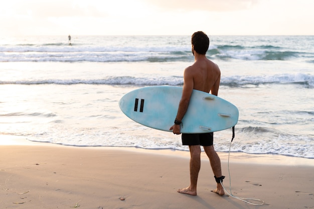 Il giovane uomo caucasico si alza presto per fare surf all'alba