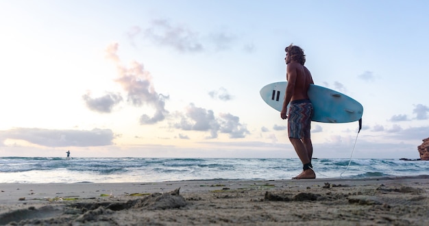 Il giovane uomo caucasico si alza presto per fare surf all'alba