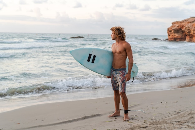 Il giovane uomo caucasico si alza presto per fare surf all'alba