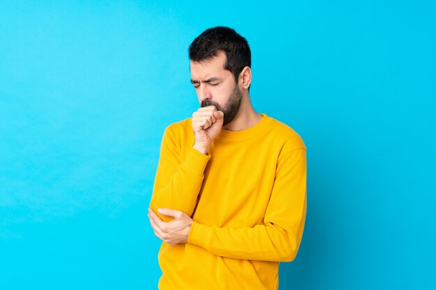 Il giovane uomo caucasico sopra la parete blu isolata sta soffrendo di tosse e si sente male