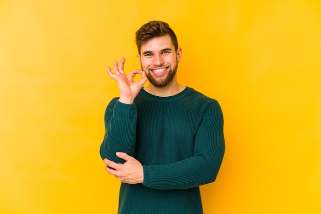 Il giovane uomo caucasico strizza l'occhio e tiene un gesto giusto con la mano.