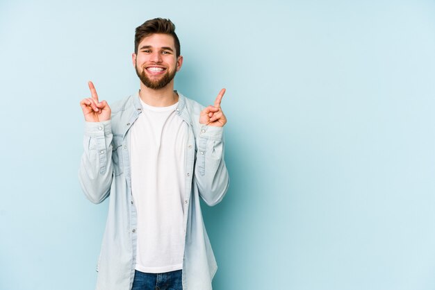 Il giovane uomo caucasico sull'azzurro indica con entrambe le dita anteriori su mostrando uno spazio vuoto.