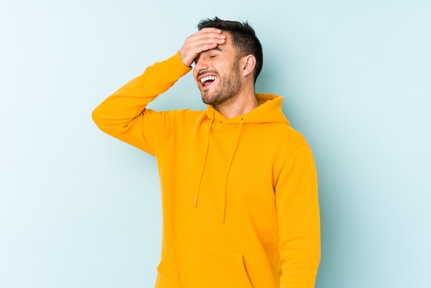 Il giovane uomo caucasico sull'azzurro ride con gioia mantenendo le mani sulla testa. Concetto di felicità.