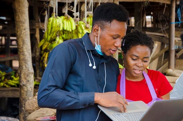 Il giovane uomo d'affari africano si sente eccitato mentre mostra a una donna del mercato alcune informazioni sul suo laptop.