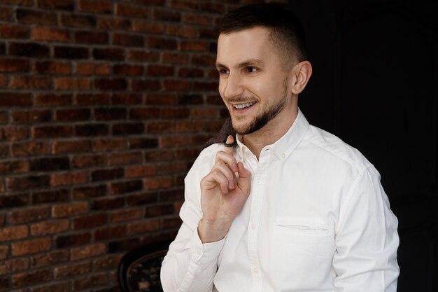 Il giovane uomo d'affari alla moda in camicia bianca sta sorridendo e tenendo una giacca sul dito