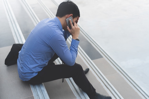 Il giovane uomo d&#39;affari asiatico che si siede sulle scale che parla sul telefono sta sollecitando.