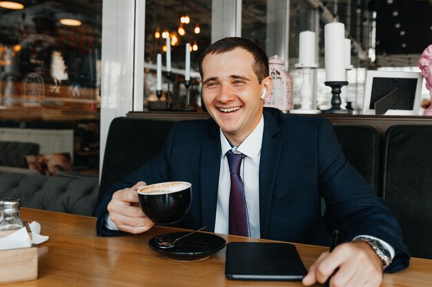 Il giovane uomo d'affari bello sorride e beve il caffè in un caffè. uomo in giacca e cravatta con caffè.