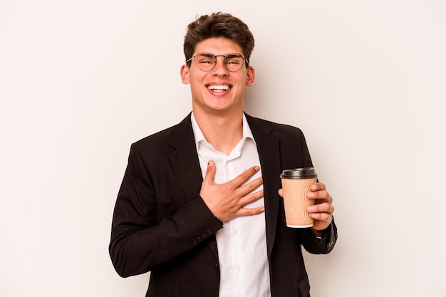 Il giovane uomo d'affari caucasico che tiene il caffè da asporto isolato su sfondo bianco ride ad alta voce tenendo la mano sul petto