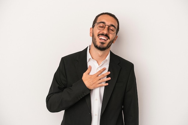 Il giovane uomo d'affari caucasico isolato su sfondo bianco ride forte tenendo la mano sul petto.