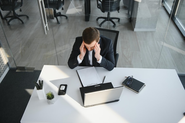 Il giovane uomo d'affari depresso che tiene la testa tra le mani ha un problema con un laptop sulla scrivania Un ragazzo ha commesso un errore in un lavoro