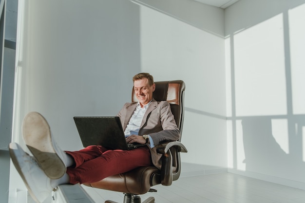 Il giovane uomo d'affari di successo sta lavorando al computer portatile con i piedi alzati e sorridendo