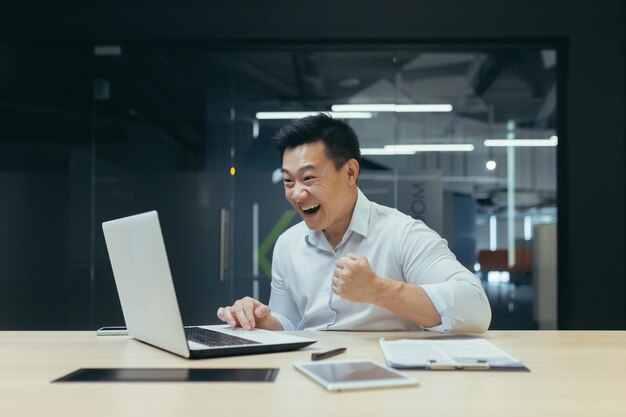 Il giovane uomo d'affari maschio asiatico è felice di un progetto finanziario di successo in cui lavora