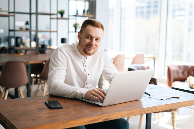 Il giovane uomo d'affari sorridente felice sta scrivendo sul computer portatile alla scrivania in ufficio a casa