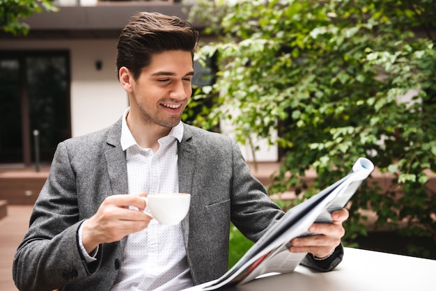 Il giovane uomo d'affari sorridente si è vestito in vestito che beve caffè