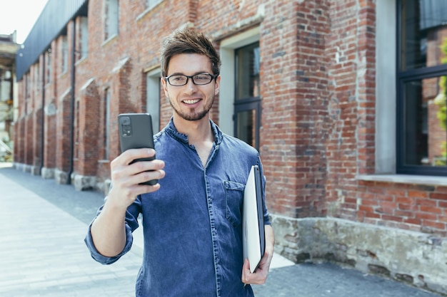 Il giovane uomo d'affari usa il telefono fuori dall'ufficio uomo felice e sorridente con lo smartphone