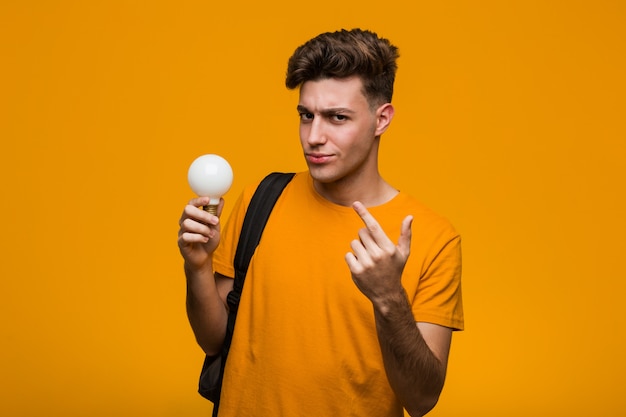 Il giovane uomo dello studente che tiene una lampadina ha colpito lo spazio della copia della tenuta sulla palma.