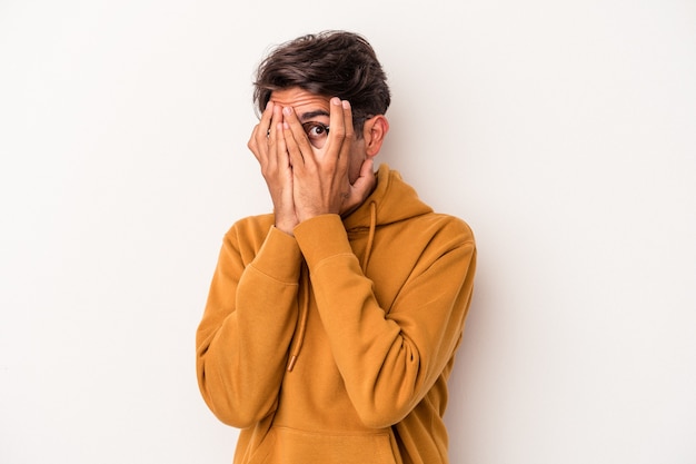 Il giovane uomo di razza mista isolato su sfondo bianco lampeggia tra le dita spaventato e nervoso.