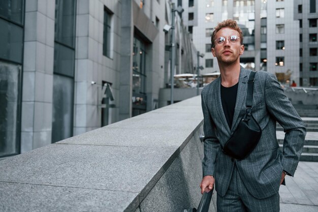 Il giovane uomo elegante in bei vestiti è all'aperto in città durante il giorno