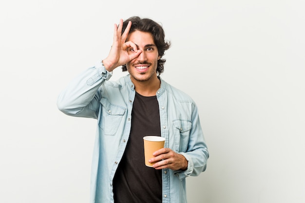 Il giovane uomo freddo che beve un caffè ha eccitato mantenendo il gesto giusto sull'occhio.