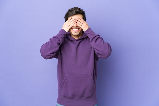 Il giovane uomo freddo copre gli occhi con le mani, sorride ampiamente aspettando una sorpresa