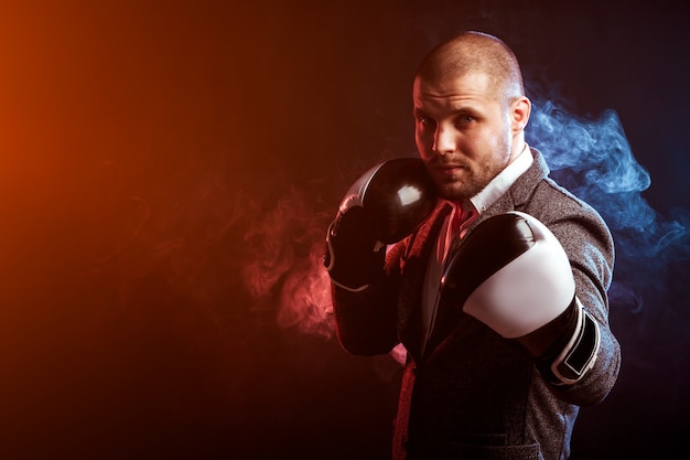 Il giovane uomo intelligente in guanti da boxe bianchi si incastra contro un muro di fumo rosso e blu