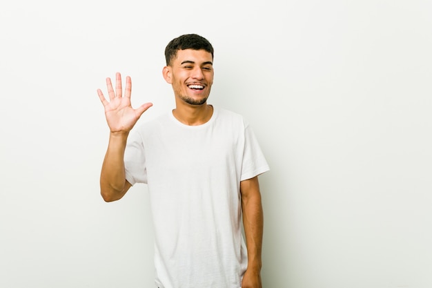 Il giovane uomo ispanico strizza l'occhio e tiene un gesto giusto con la mano.